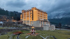 A multi-story hotel with a prominent 'VIVANTA' sign, surrounded by a traditional courtyard with a small pagoda-like structure and a red bridge. - Vivanta Tawang (Tawang)