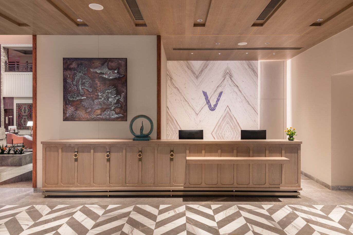 Un área de recepción con un muro con diseño de mármol, un cuadro abstracto grande y un mostrador de madera con dos parlantes negros.