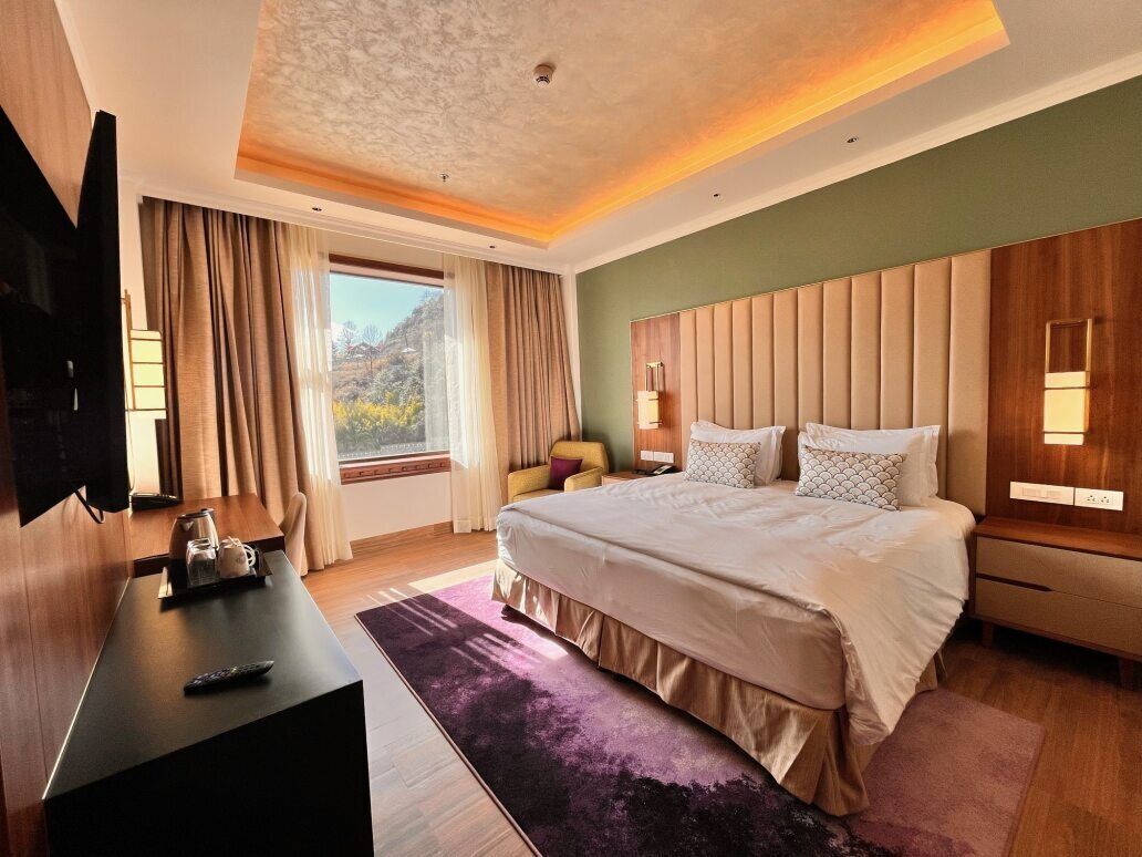 Une chambre d’hôtel moderne dotée d’un grand lit, d’une télévision à écran plat, d’un bureau avec une télécommande et d’une fenêtre avec des rideaux.