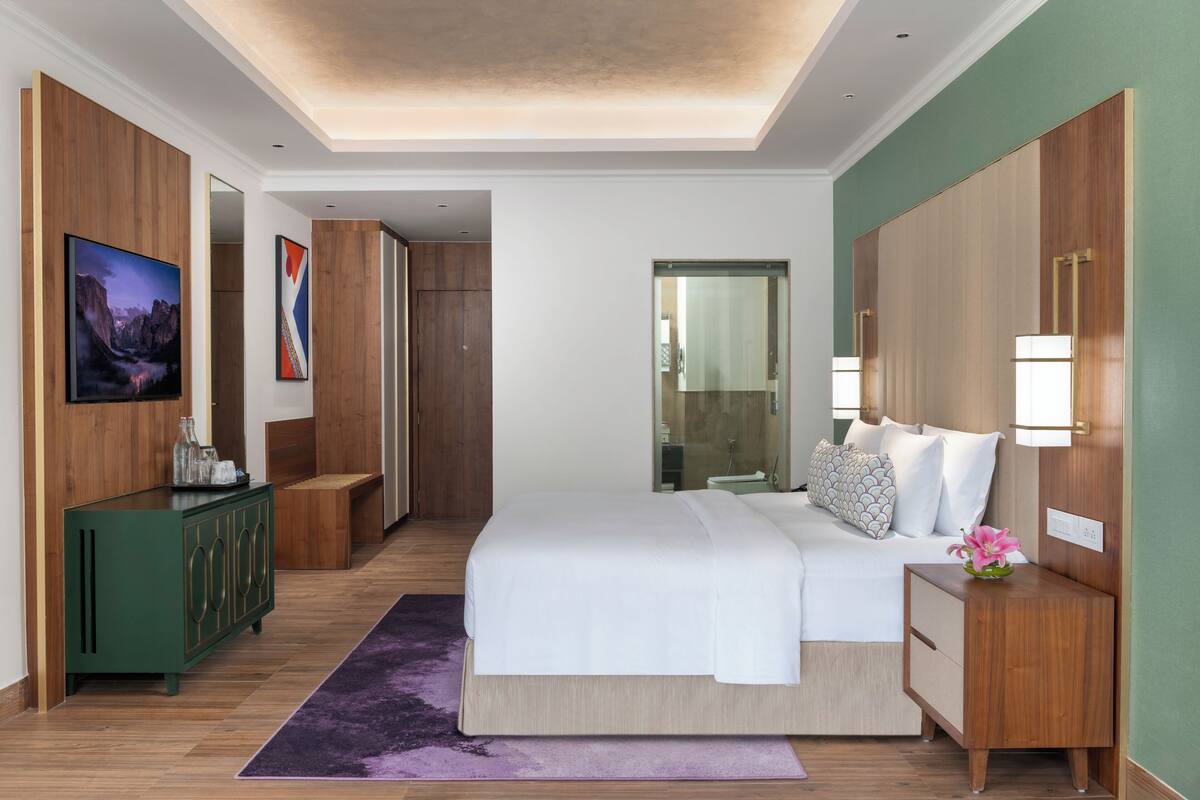 A modern hotel room with a large bed, a green cabinet, a purple rug, and a mirror on the wall.