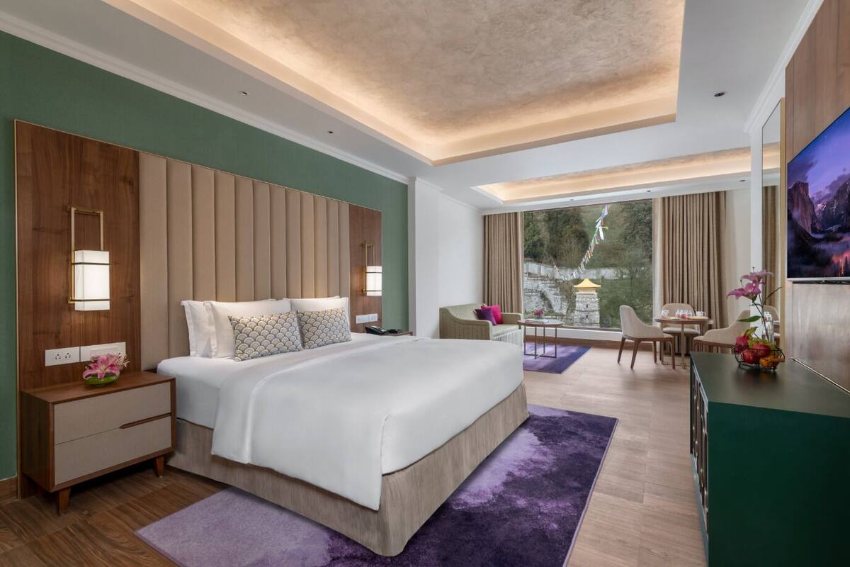 A modern hotel room with a large bed, a desk, a TV, and a view of a mountainous landscape.
