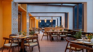 A restaurant with multiple tables and chairs, a bar area, and large windows offering a view of the cityscape. - Vivanta Tawang (Tawang)