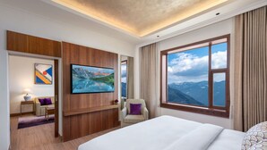 A hotel room with a large bed, a TV mounted on the wall, a chair, a small table, and a window with a mountain view. - Vivanta Tawang (Tawang)