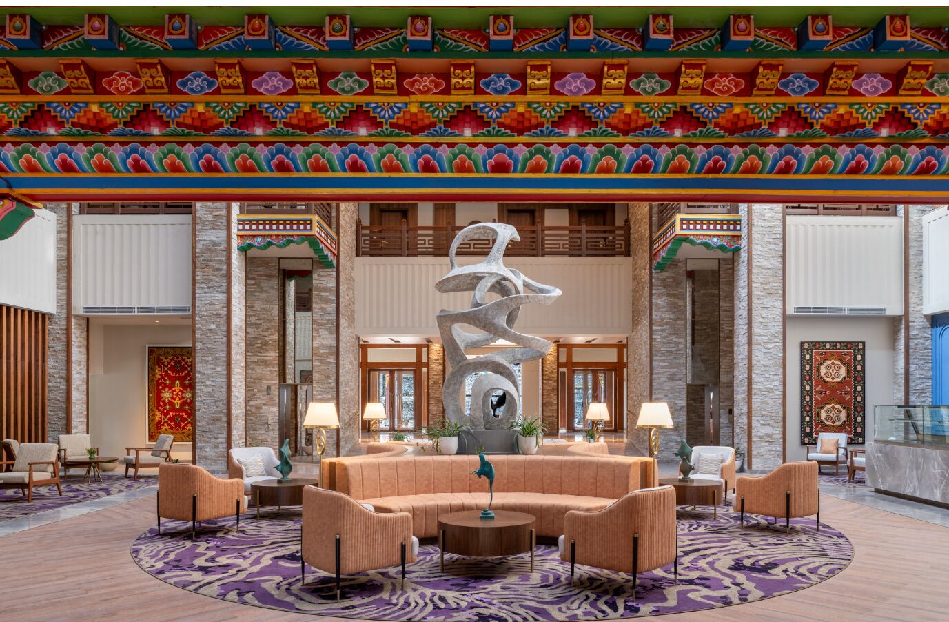A lobby with a central seating area, a large abstract sculpture, and a colorful ceiling design.