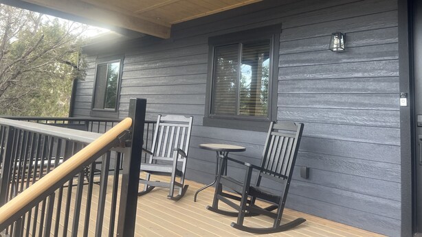 Une terrasse en bois avec une balustrade, une chaise berçante, une table et une fenêtre avec des stores.