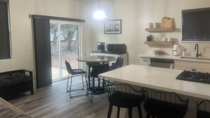 Une cuisine moderne dotée d’un îlot central, d’un coin repas avec des chaises et d’une vue sur l’extérieur grâce à une porte vitrée.