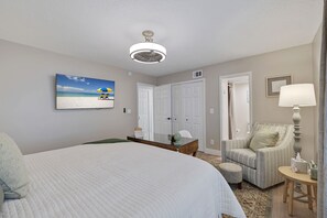A hotel room with a large bed, a desk, a chair, a lamp, and a painting of a beach scene. - Cypress & Sun on Gulf – Water Views, Beach Access, Fishing Dock & Coastal Comfort (Indian Rocks Beach)