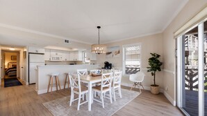 Een moderne keuken met witte kastjes, een centraal kookeiland met barkrukken, en een eethoek met een tafel en stoelen.