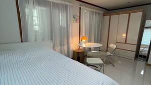 A hotel room with a large bed, a small round table with a lamp, a chair, and a wardrobe.