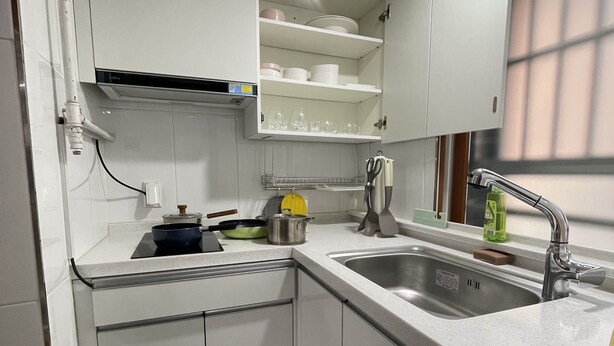 A compact kitchen with white cabinets, a stainless steel sink, and a window with blinds.