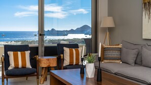 Una sala de estar moderna con vista al océano, que incluye un sofá, sillones, una mesita de centro y una lámpara.