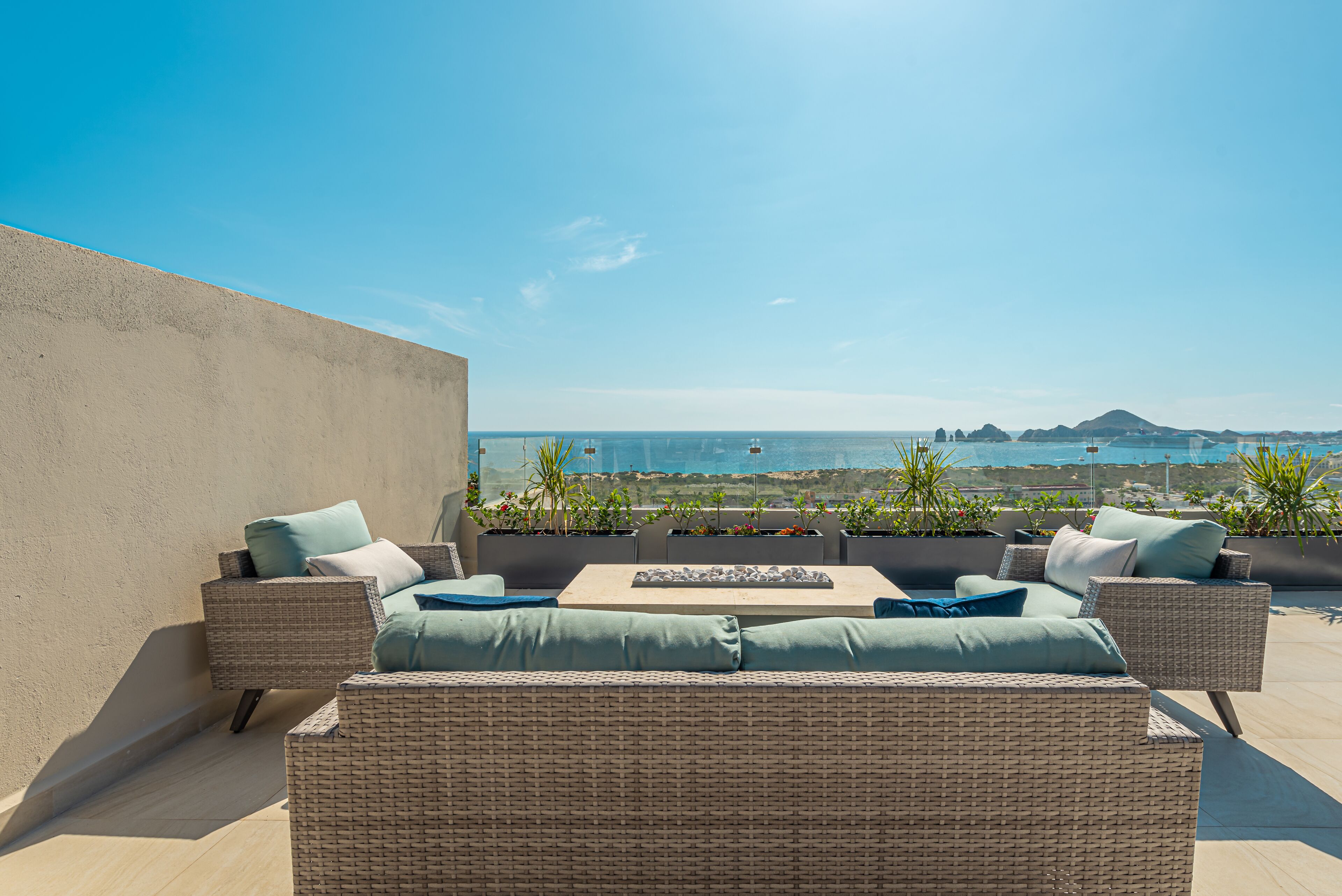 A rooftop terrace with wicker furniture, a coffee table, and potted plants.