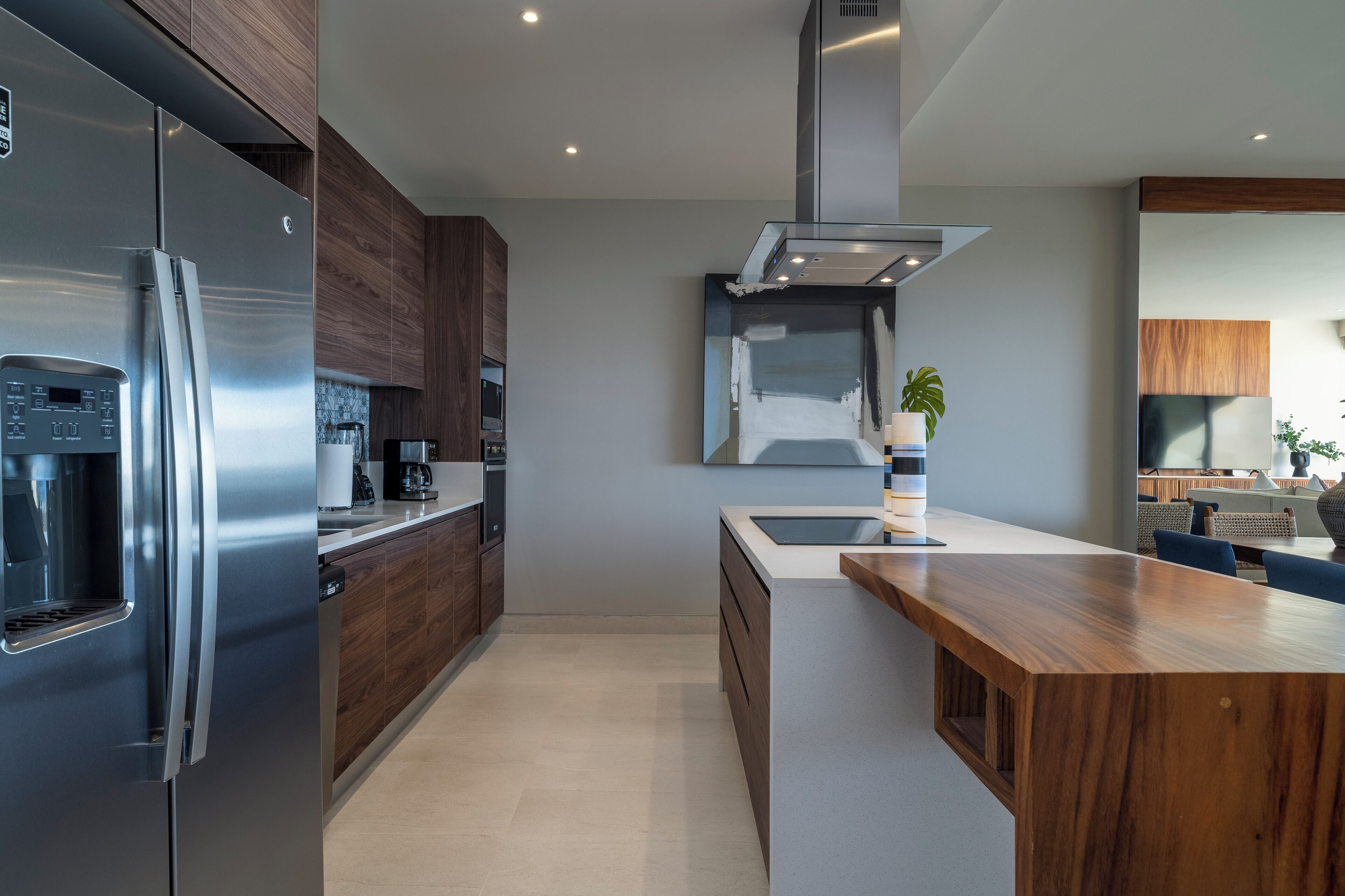A modern kitchen with a stainless steel refrigerator, wooden cabinets, a central island, and a built-in stove.