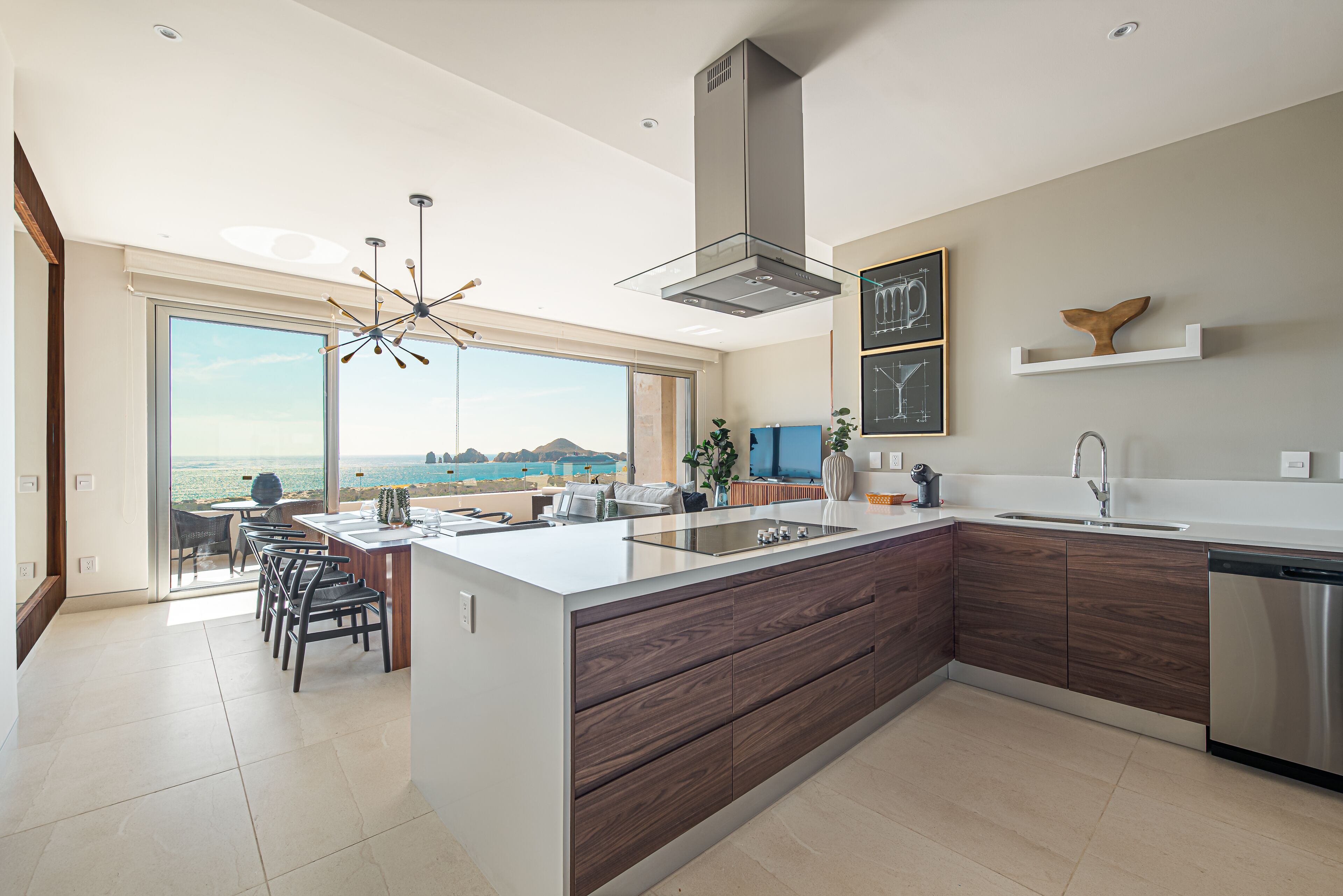 A modern kitchen with a large island, a view of the sea, and a dining area with chairs.