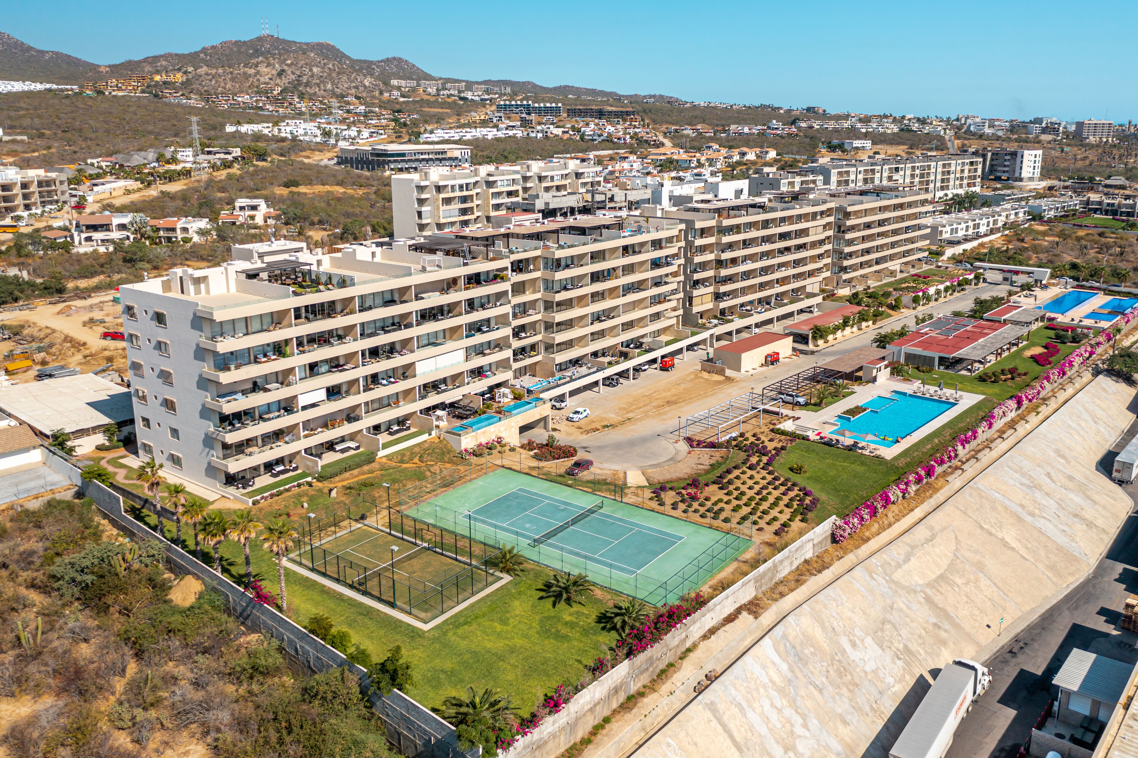 A multi-story residential building with balconies, a tennis court, and a swimming pool.