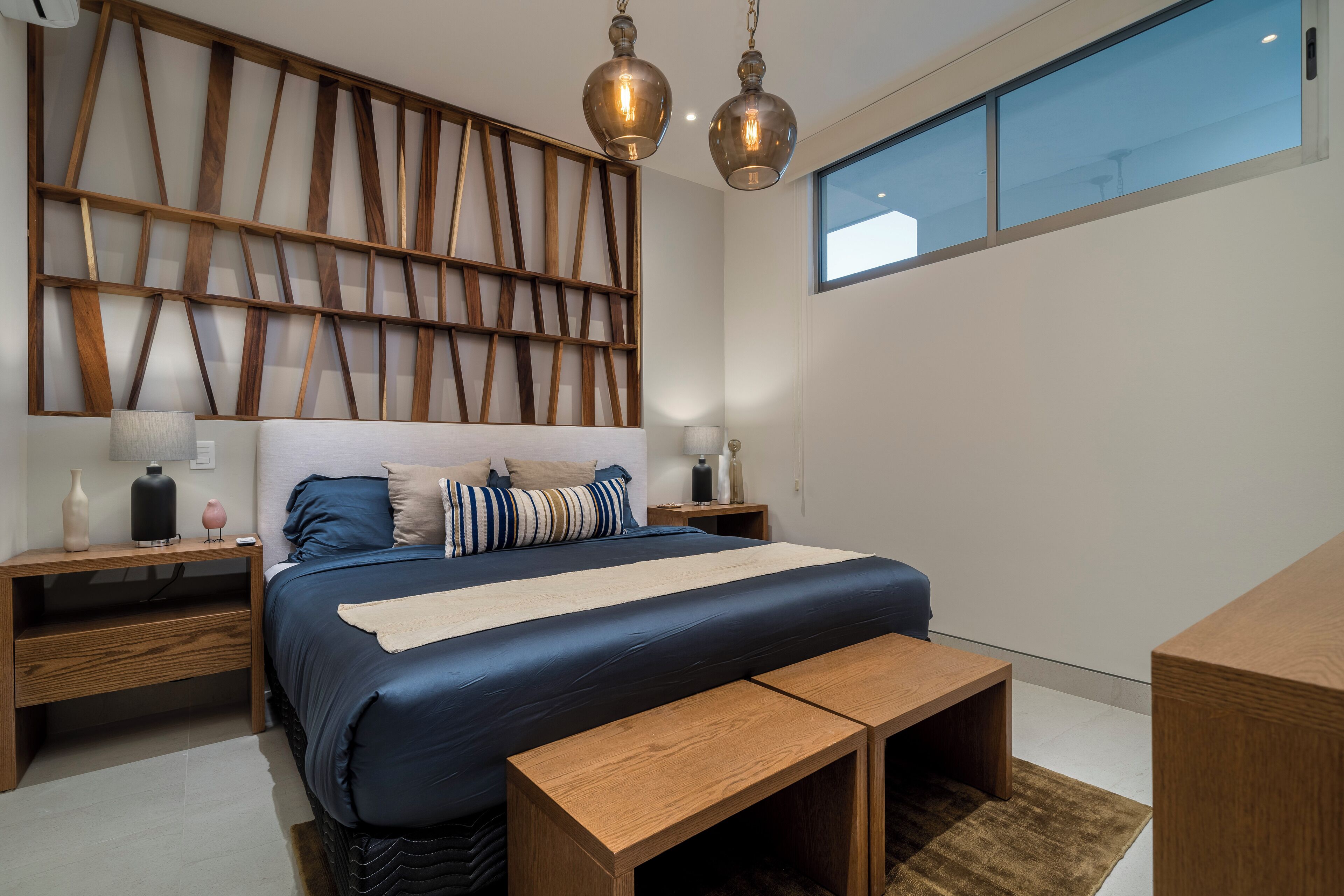 A modern bedroom with a large bed, wooden headboard, bedside tables, and a large window.