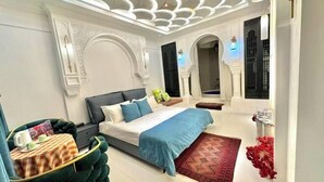 A modern bedroom with a large bed, a small table with a chair, and a decorative ceiling. - Silk Road Lodges (Turpan)