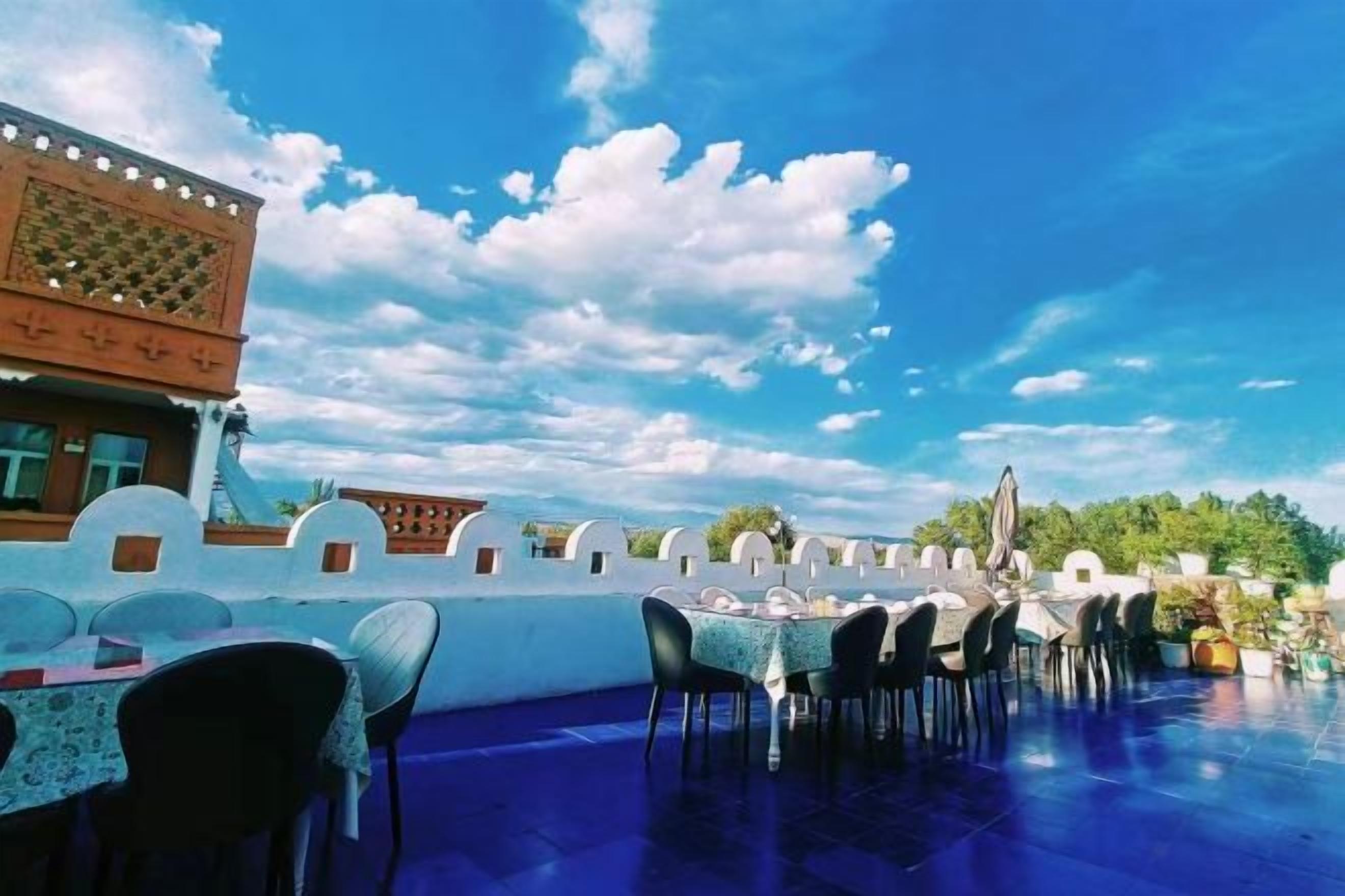 An outdoor dining area with tables and chairs, a clear blue sky, and a building with traditional architecture.