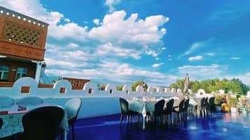 An outdoor dining area with tables and chairs, a clear blue sky, and a building with traditional architecture.