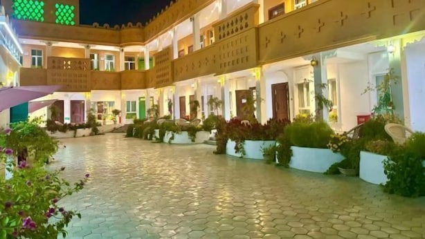 A courtyard with a tiled floor, surrounded by buildings with balconies and potted plants. - Silk Road Lodges (Turpan)