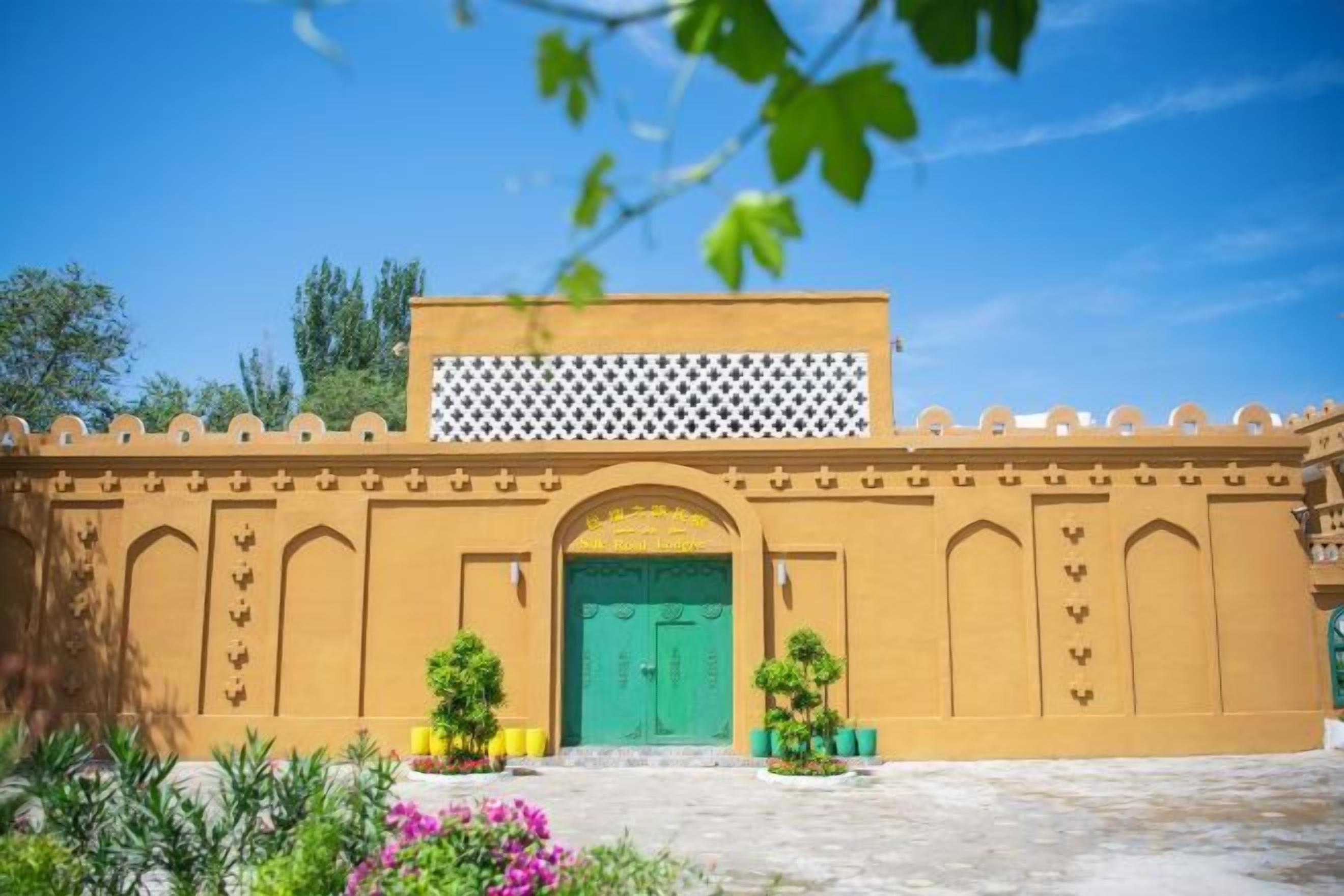 A building with a green door, a white lattice structure above, and a courtyard with plants.