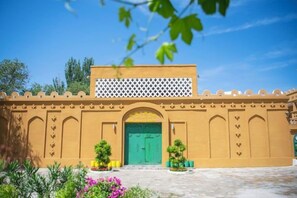 A building with a green door, a white lattice structure above, and a courtyard with plants. - Silk Road Lodges (Turpan)
