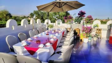 An outdoor dining area with a long table set for multiple guests, surrounded by chairs, and an umbrella providing shade.