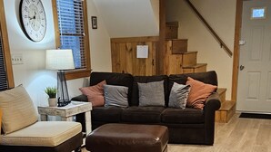 En stue med sofa, skammel og et ur på væggen.