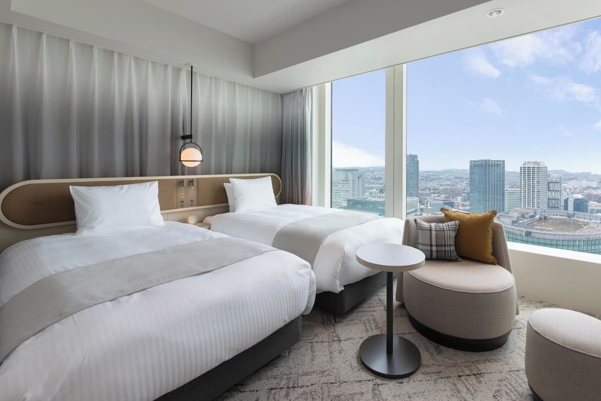 Une chambre d’hôtel avec deux lits, une table ronde et une vue sur le paysage urbain.