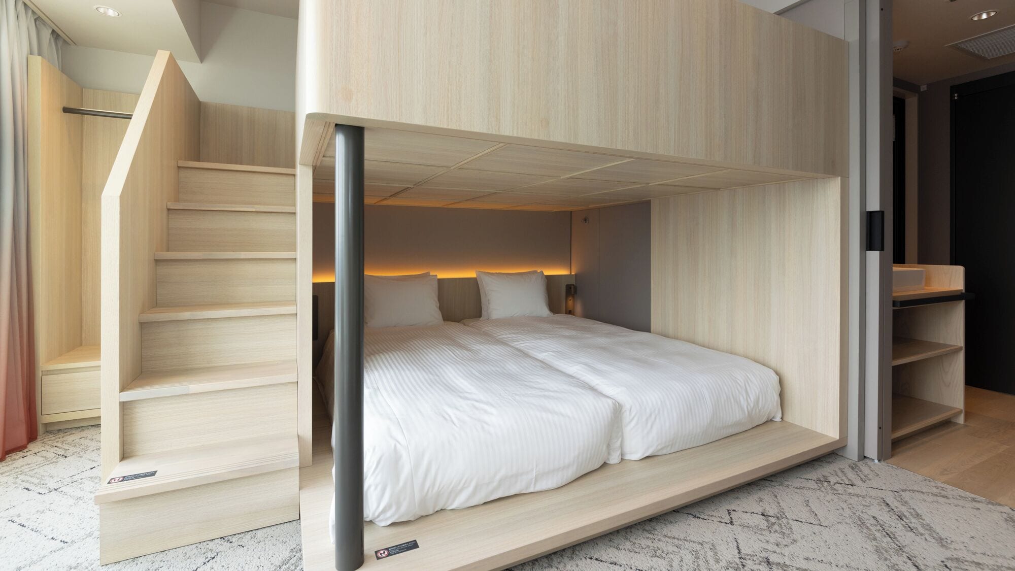 A modern hotel room with a built-in bed, a staircase, and a small seating area.