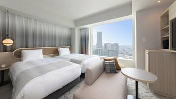 Une chambre d’hôtel avec deux lits, un bureau, une chaise, une télévision et une grande fenêtre donnant sur la ville.