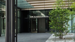 The entrance to the Keikyuu EX Hotel with a modern glass facade, a tree in the foreground, and a clean, tiled pavement. - KEIKYU EX HOTEL MINATOMIRAI YOKOHAMA (Yokohama)