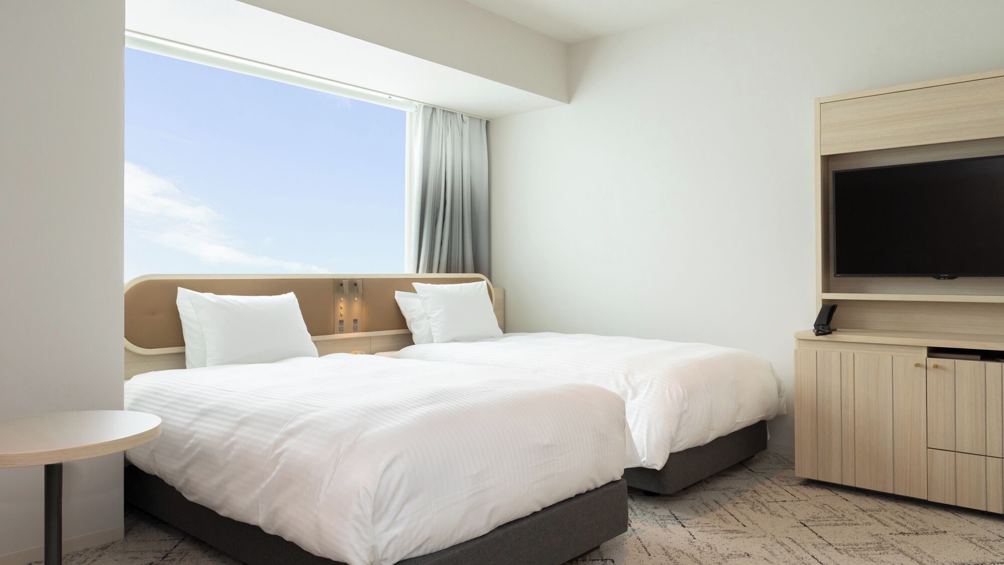 Une chambre d’hôtel avec un lit, une télévision, une petite table et une fenêtre avec des rideaux.