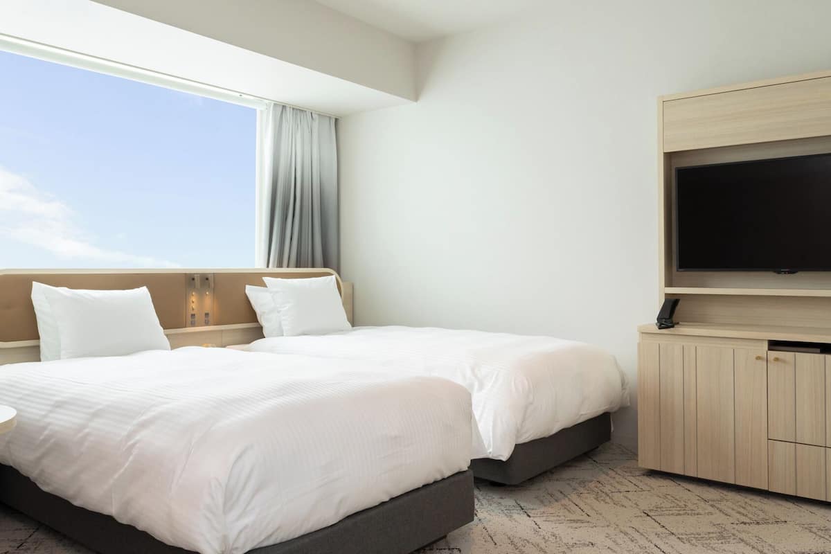 Une chambre d’hôtel avec un lit, une télévision, une petite table et une fenêtre avec des rideaux.