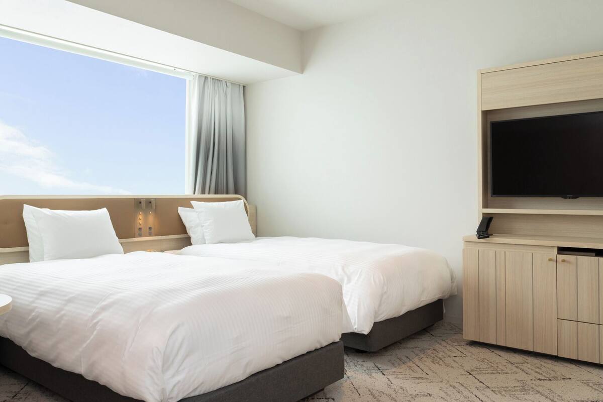 Une chambre d’hôtel avec un lit, une télévision, une petite table et une fenêtre avec des rideaux.
