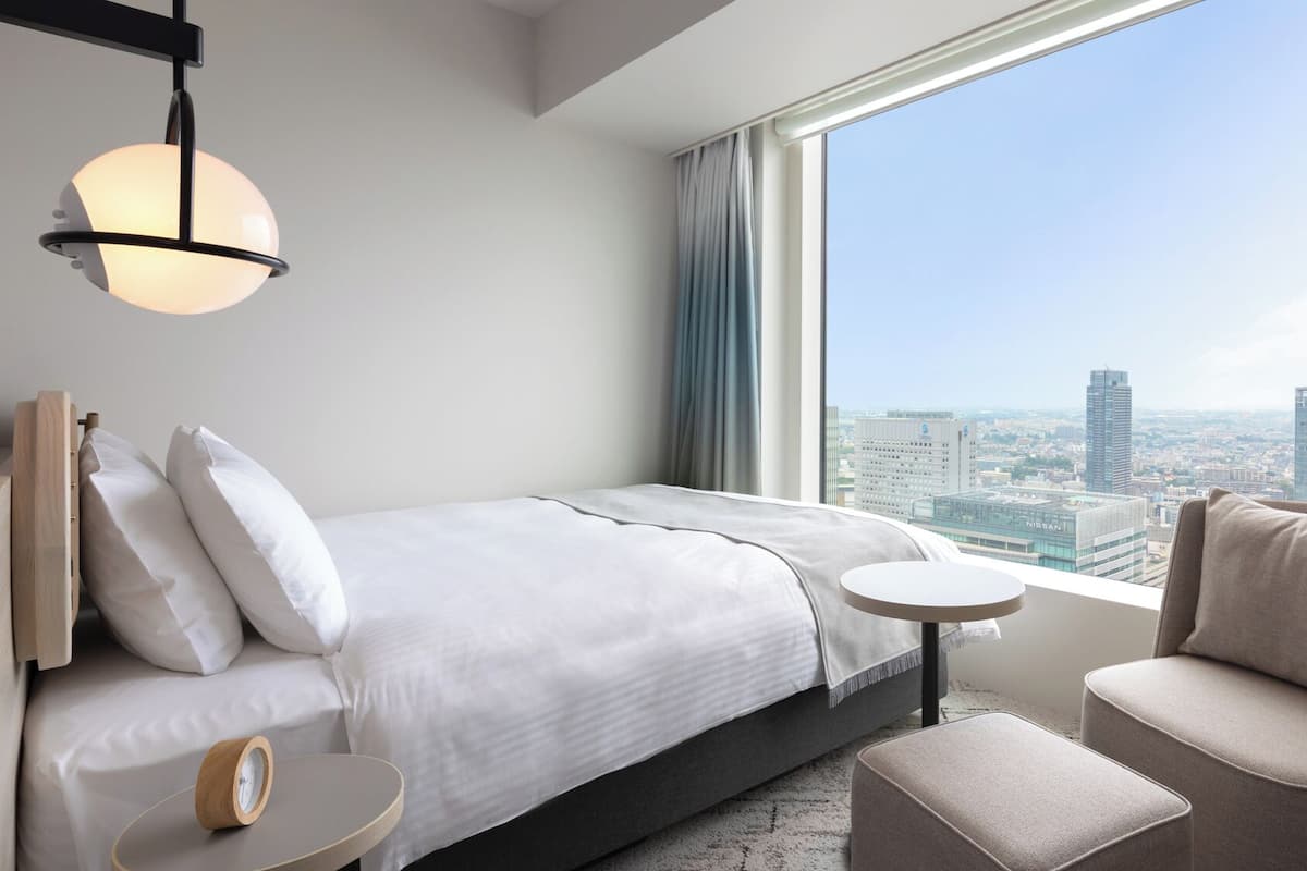 Une chambre d’hôtel moderne équipée d’un lit, d’une table ronde, d’une chaise et d’une grande fenêtre donnant sur la ville.