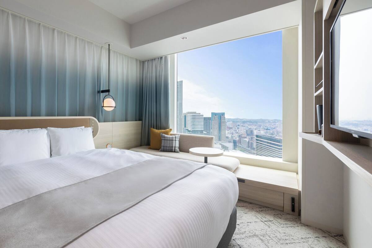 Une chambre d’hôtel avec un grand lit, une petite table, un canapé et une vue sur la ville.