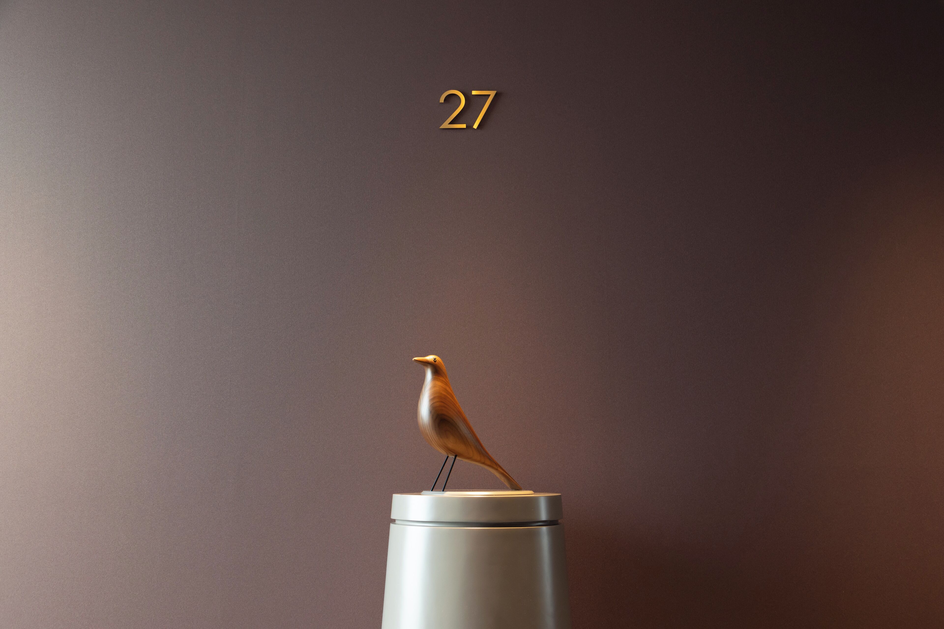 A minimalist design with a bird sculpture on a cylindrical object against a plain background.