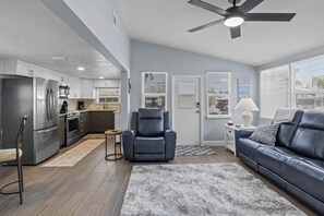A modern kitchen with stainless steel appliances, a dining area with a leather chair, and a living room with a sofa and a ceiling fan. - 3713 115th St.Ct.W. - Mobile home Bradenton - 2 Bedroom/ 2 Bath , maximum occupancy of 4 people. Distance to the Beach: 5 min by car. (Bradenton)