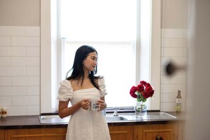A person in a white dress standing in a kitchen with a window, a sink, and a vase with red flowers on the counter. - COUNTRY STYLE LOUISA 4.5🌟 Gawler-Adelaide-Barossa🚞Adelaide Style Accommodation (Gawler)
