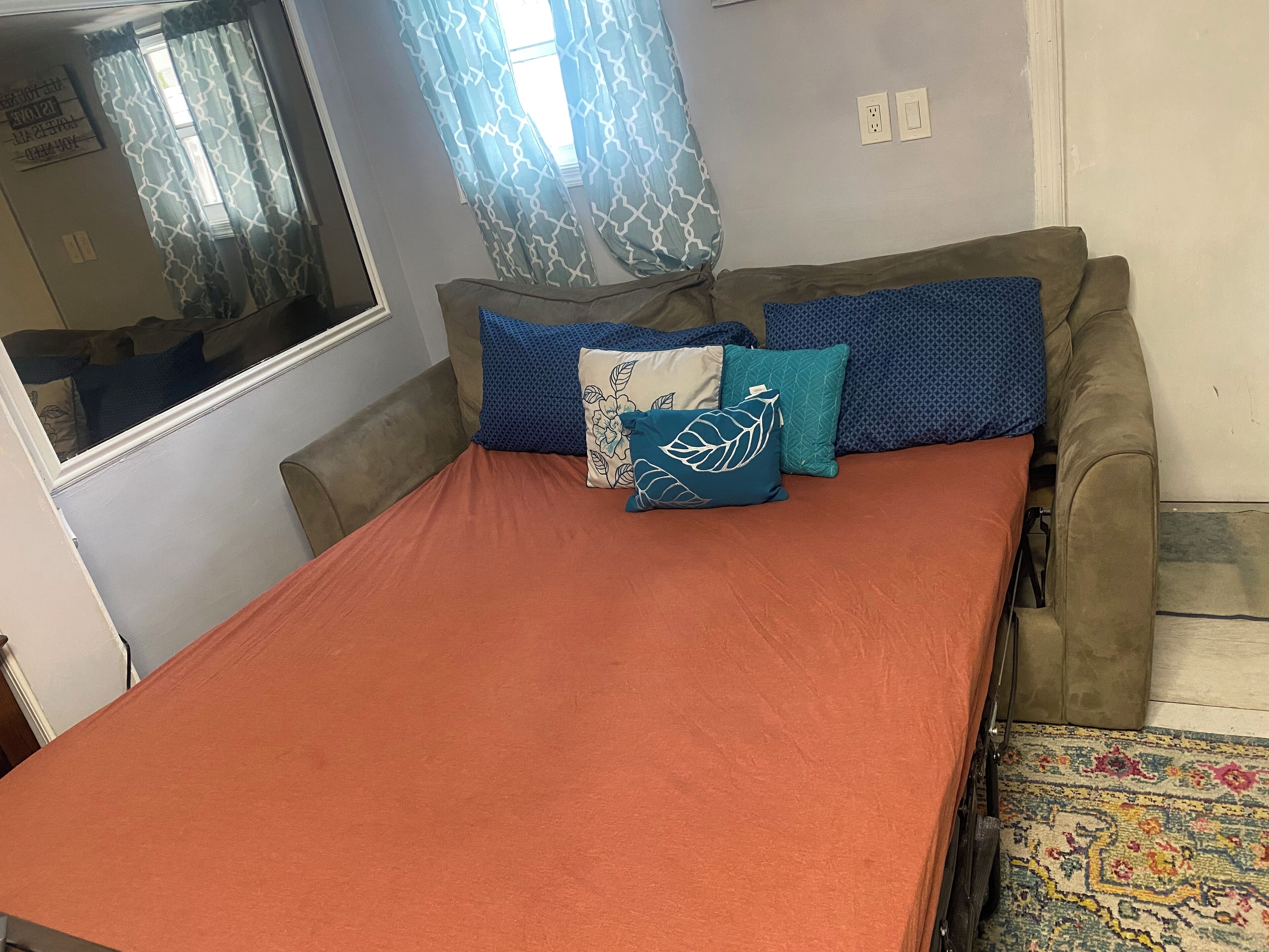 Un espace de vie compact comprenant un canapé-lit, une petite table et une fenêtre agrémentée de rideaux à motifs.