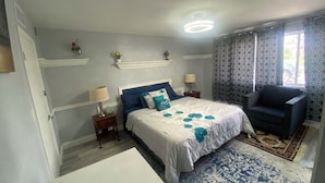 A bedroom with a bed, two bedside tables, a chair, a window with curtains, and a patterned rug.