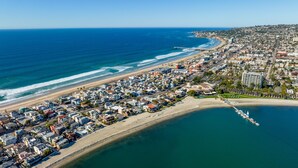Vista aérea de un pueblo costero con playa, muelle y una combinación de edificios residenciales y comerciales.