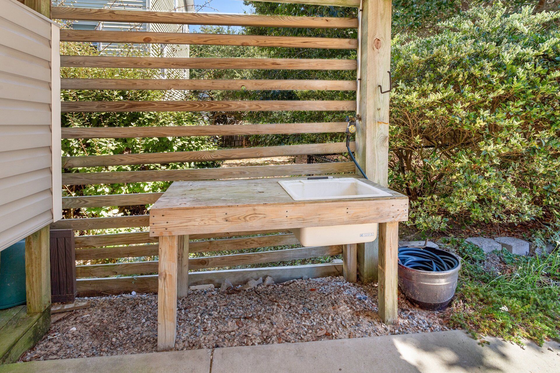 A wooden outdoor bench with a white sink, surrounded by gravel and greenery.