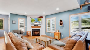 A living room with a fireplace, leather sofas, a coffee table, and a television mounted above the fireplace. - Mighty Duck: Hot Tub, Fire Pit, Game Room, Duck OBX (Duck)