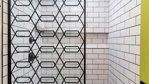 Une salle de bain aux murs recouverts de carreaux blancs et dotée d’une cloison en métal noir aux motifs géométriques.