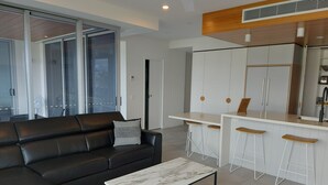 Ein modernes Wohnzimmer mit einem schwarzen Ledersofa, einem Marmortisch und einer Küchenzeile mit weißen Schränken und Holzschemeln.