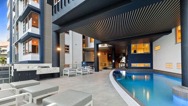 Ein moderner Poolbereich mit Liegestühlen, einer Bar und einer überdachten Lounge.