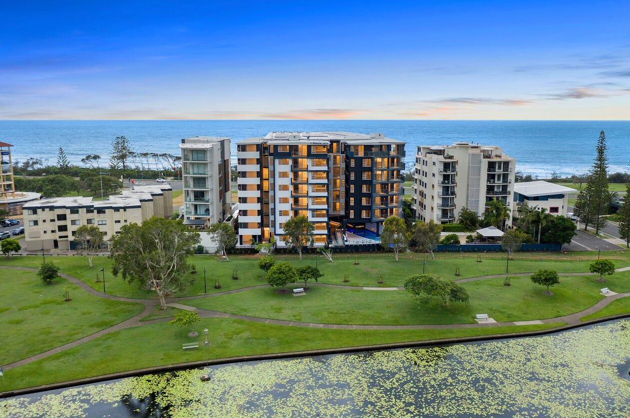 A multi-story hotel with a central courtyard, surrounded by greenery and a view of the ocean.