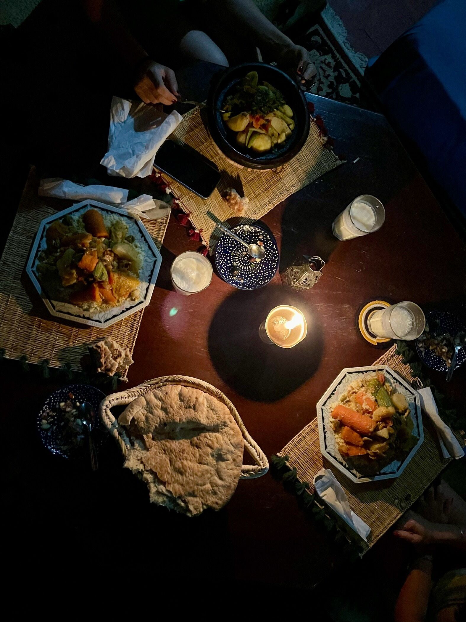 Una mesa de comedor con diversos platos y una vela, rodeada de individuales tejidos y una cesta de mimbre.